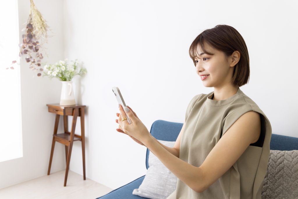ソファーに座ってスマホを操作する若い女性の様子