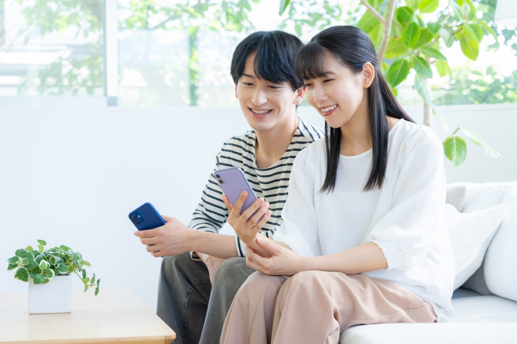 リビングでスマホを見る若いカップルの様子