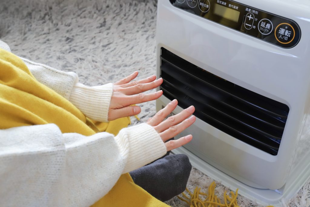 ファンヒーターで温まっている女性