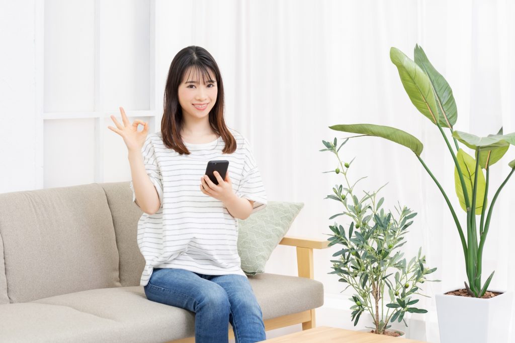 ソファーに座ってスマホを操作する若い女性の様子