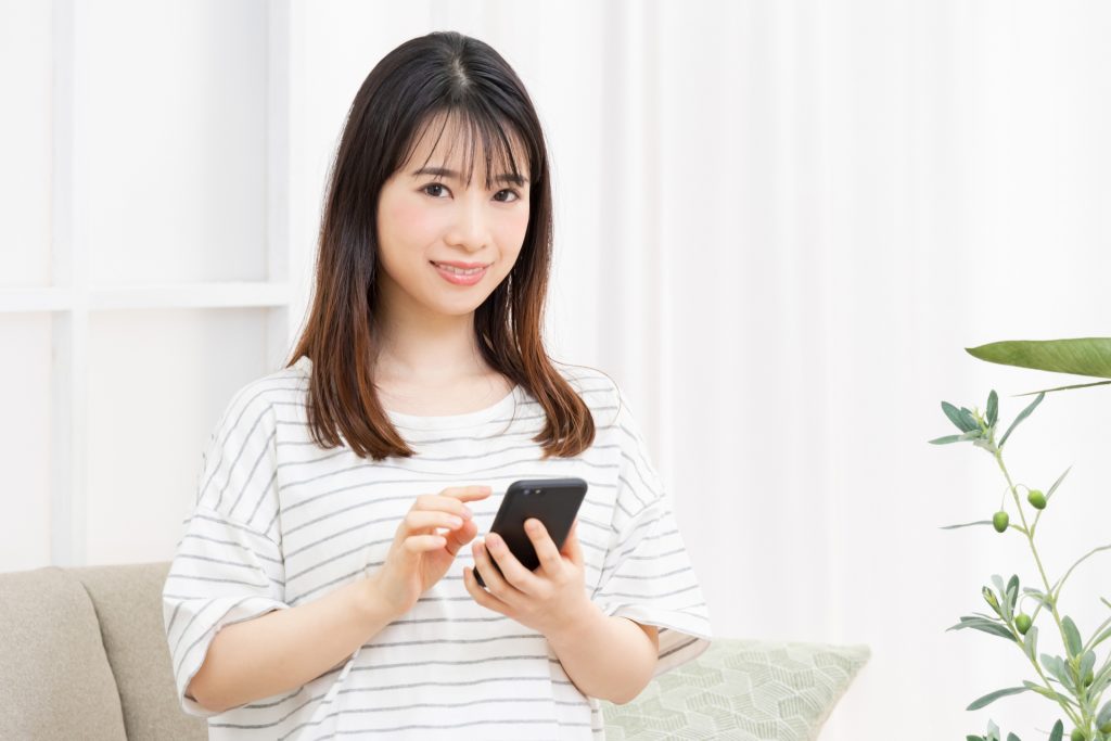 ソファに座ってスマホを操作する若い女性の様子